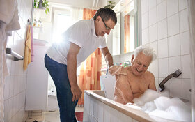 Ein Mann hilft seinem älteren Angehörigen beim Waschen in der Badewanne.