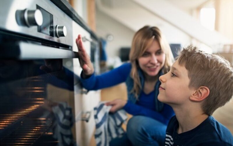 Mutter erklärt ihrem Sohn, dass der Backofen heiß ist und zeigt so feste Grenzen im Haushalt auf.