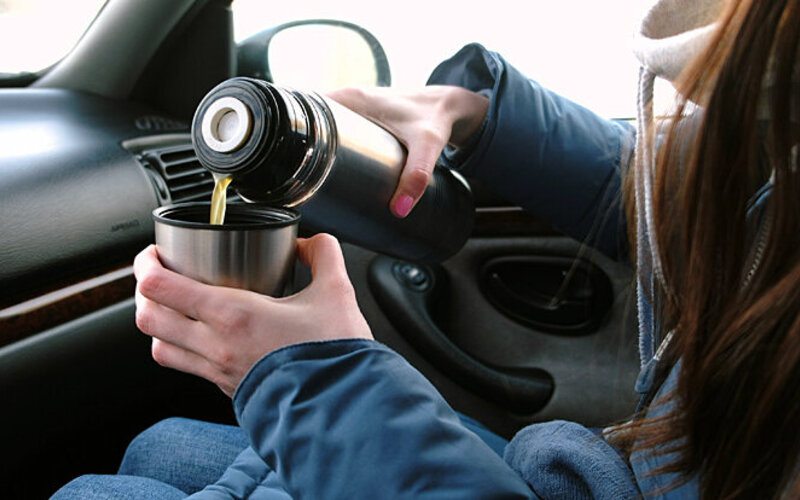Eine Frau gießt sich im Auto aus einer Thermoskanne Ingwertee gegen Reiseübelkeit ein.