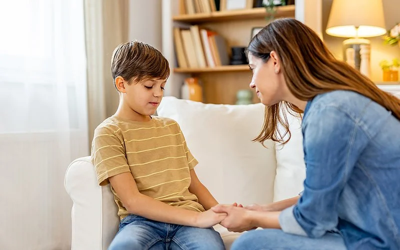 Eine Mutter sitzt mit ihrem Sohn auf dem Sofa und hält seine Hände.