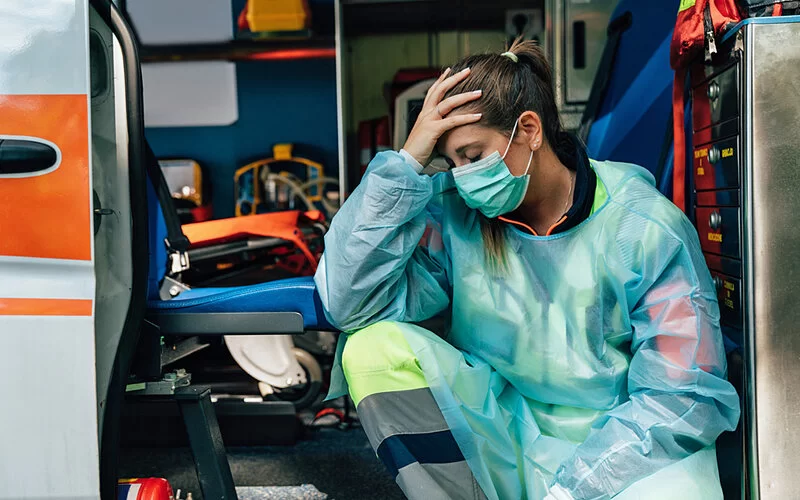 Eine Sanitäterin fasst sich mit der Hand erschöpft an den Kopf.