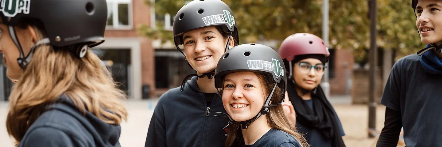 Eine Gruppe Kinder und Jugendlicher sthen bekleidet mit schwarzen T-Shirts und Helmen auf einem Vorplatz.
