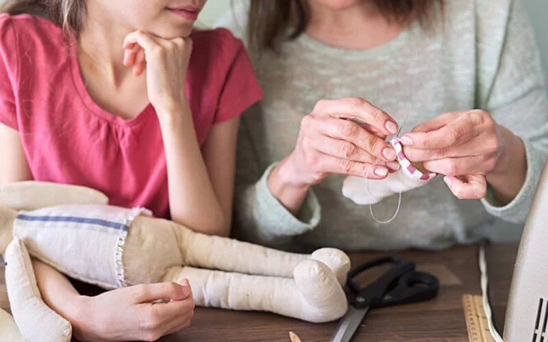 Mutter und Tochter nähen ein Stofftier aus alter Babykleidung.