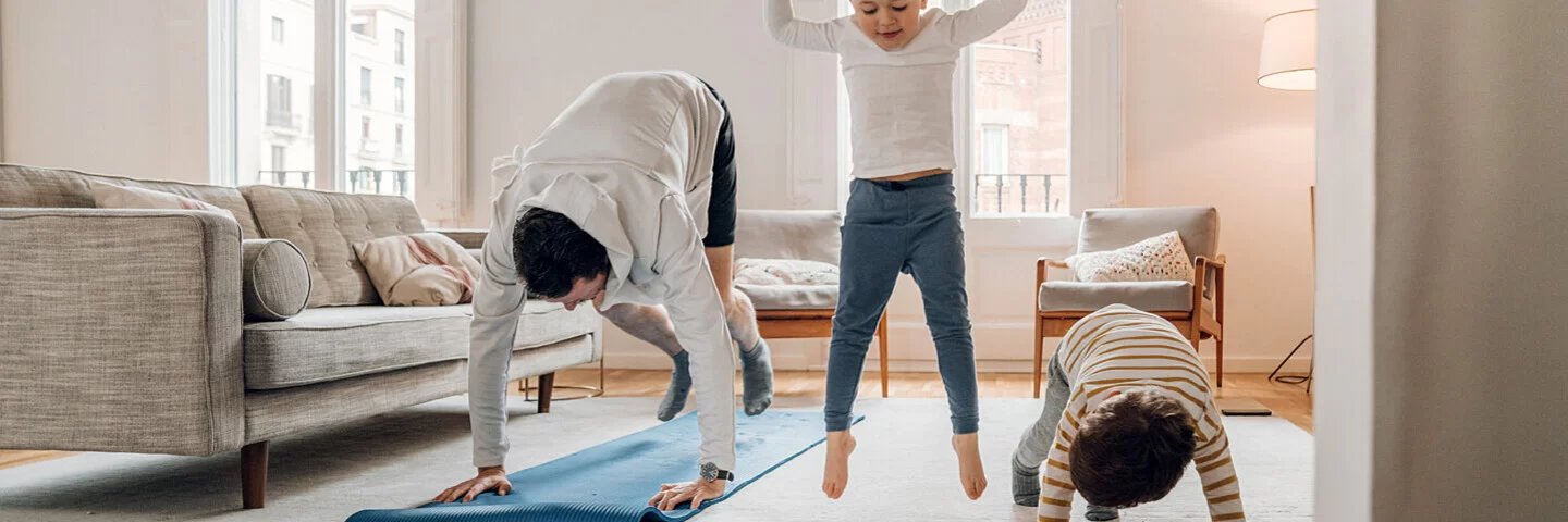 Ein Vater macht zu Hause Sport mit seinen beiden Kindern.