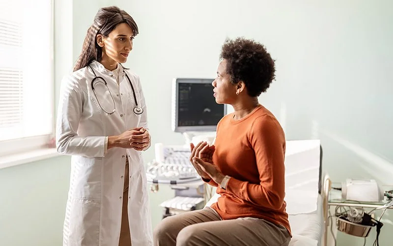 Eine Frau in einem ärztlichen Untersuchungszimmer spricht mit einer Ärztin.