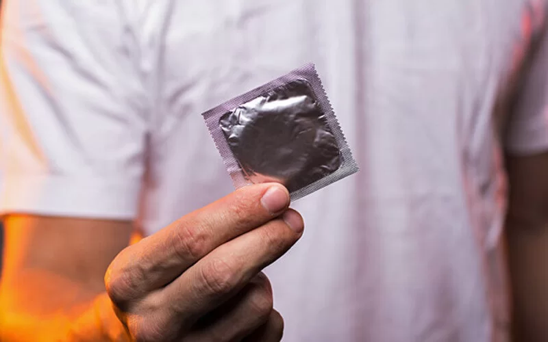 Ein Mann hält ein Kondom in die Kamera, das vor Chlamydien schützen kann.