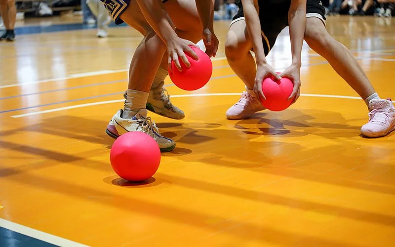 Drei weiche rote Schaumstoffbälle liegen auf dem Boden. Zwei Spieler greifen zwei von ihnen.