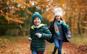 Zwei Kinder toben im herbstlichen Wald und beugen damit Erkältungen vor.