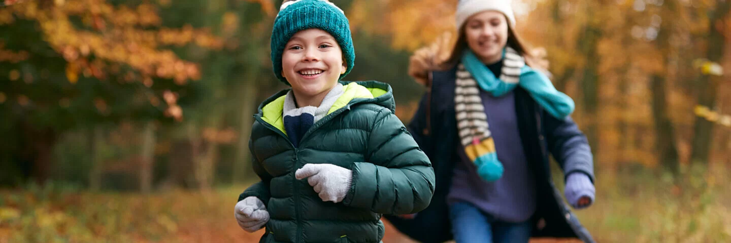 Zwei Kinder toben im herbstlichen Wald und beugen damit Erkältungen vor.