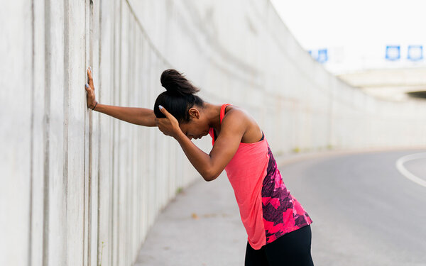 Eine Joggerin steht an einer Wand und hält sich wegen Kopfschmerzen den Kopf.