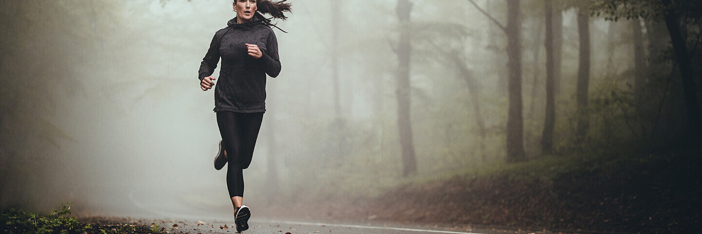 Frau erlebt ein Runner’s High beim Joggen auf einer Landstraße.