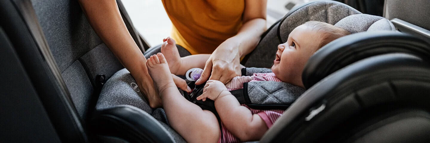 Eine Mutter setzt ihr Baby in die Sitzerhöhung im Auto und schnallt es an.