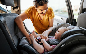 Eine Mutter setzt ihr Baby in die Sitzerhöhung im Auto und schnallt es an.
