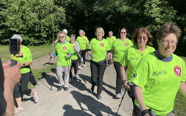 Eine Gruppe Nordic Walker läuft in grünen AOK-Shirts im Park.