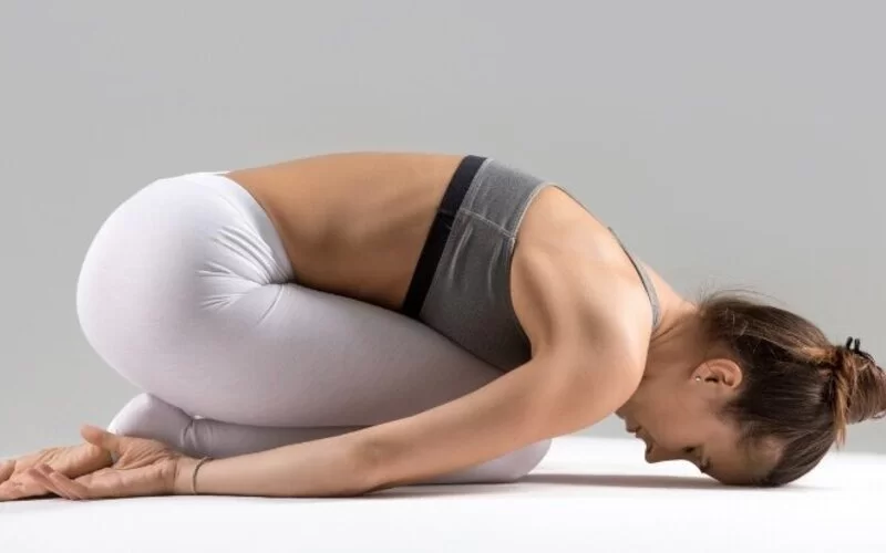 Eine Frau macht Yin Yoga und liegt in der Kindhaltung auf einer Yogamatte. 