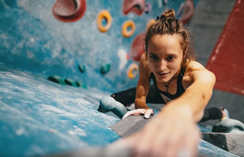 Junge, dünne Frau beim Klettern an der Boulderwand aus der Vogelperspektive.