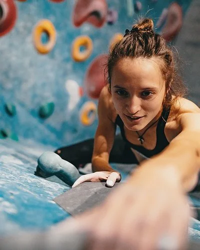 Junge, dünne Frau beim Klettern an der Boulderwand aus der Vogelperspektive.