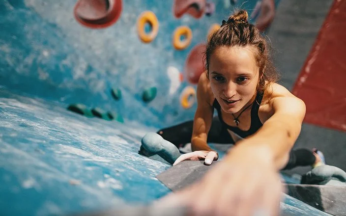 Junge, dünne Frau beim Klettern an der Boulderwand aus der Vogelperspektive.