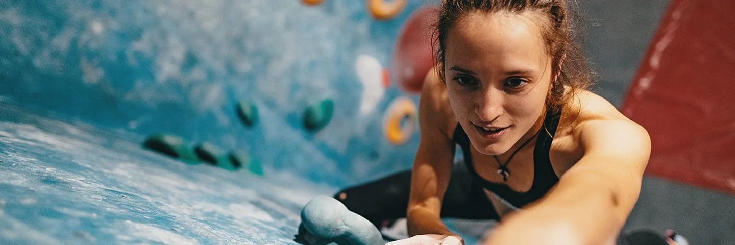 Junge, dünne Frau beim Klettern an der Boulderwand aus der Vogelperspektive.