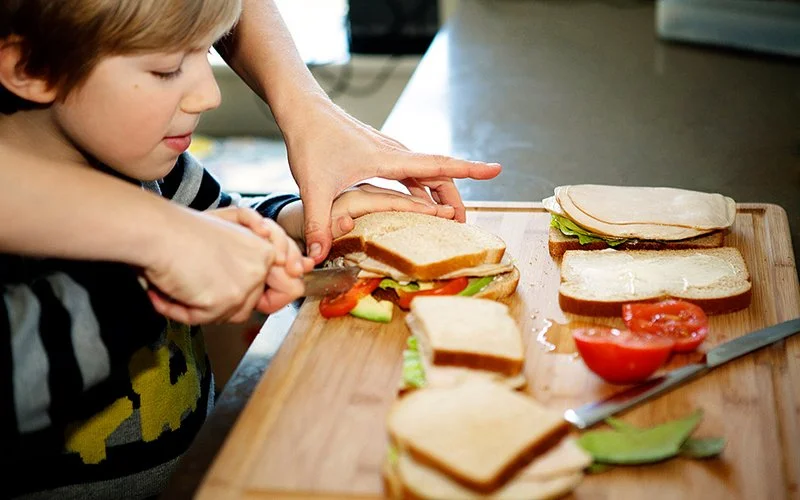 Kind und Vater schneiden Tomaten und Avocados für ein Sandwich zurecht.