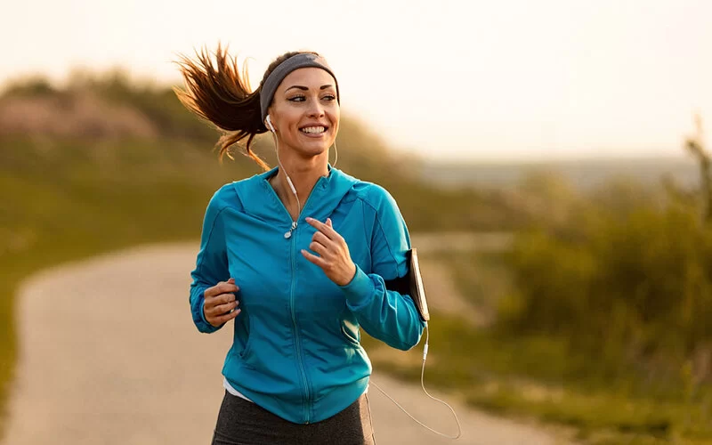 Eine junge Frau joggt fröhlich blickend einen Weg entlang.