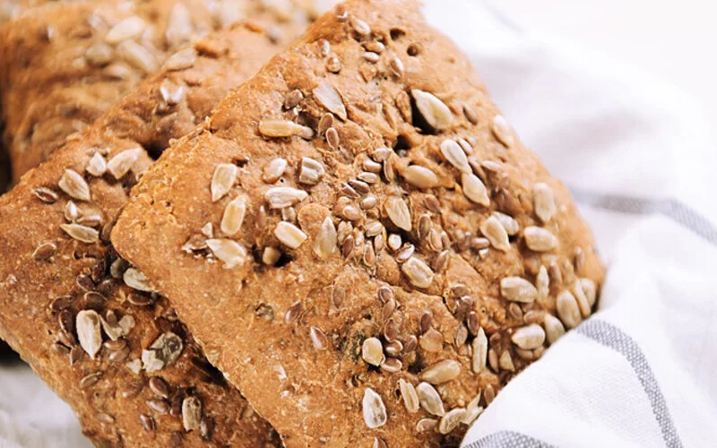 Glutenfreie Brötchen mit Sonnenblumenkernen, Leinsamen und Sesam auf einem Handtuch in einem Korb.