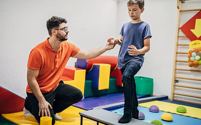 Ein Junge mit Kinderheuma ist bei einem Ergotherapeuten und macht Bewegungsübungen.