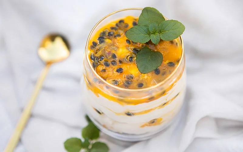 In einem Glas ist abwechselnd Quark und Passionsfrucht geschichtet. Obendrauf liegt frische Minze.