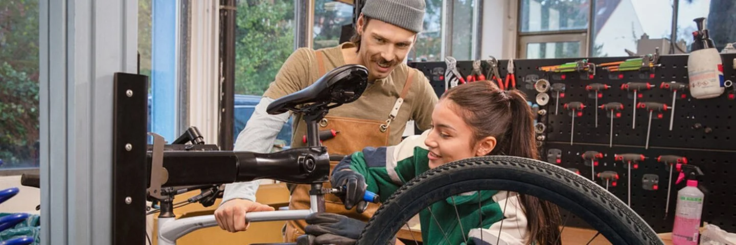 Ausbilder erklärt einer Auszubildenden die Reparatur eines Fahrrads in der Werkstatt.