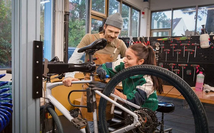 Ausbilder erklärt einer Auszubildenden die Reparatur eines Fahrrads in der Werkstatt.