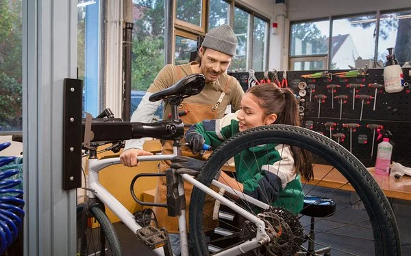 Ausbilder erklärt einer Auszubildenden die Reparatur eines Fahrrads in der Werkstatt.
