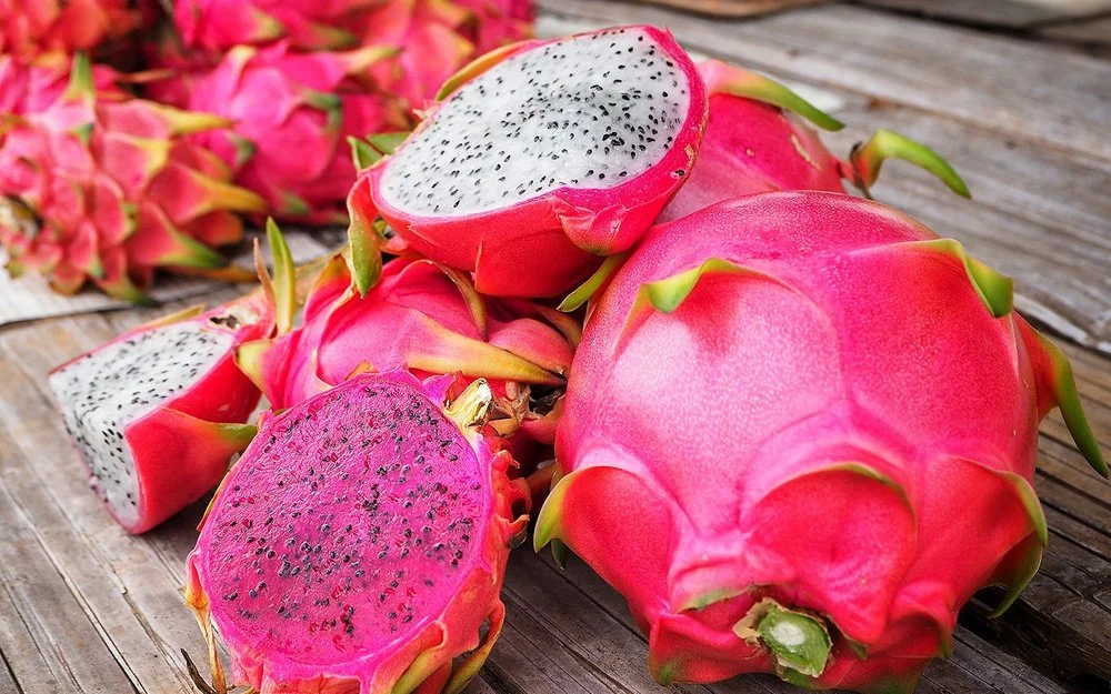 Mehrere Drachenfrüchte liegen teilweise aufgeschnitten auf einem Tisch.