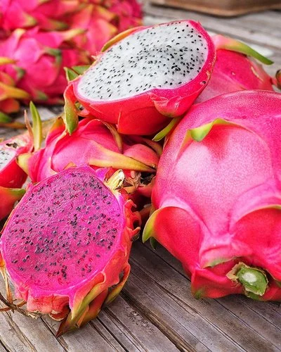 Mehrere Drachenfrüchte liegen teilweise aufgeschnitten auf einem Tisch.