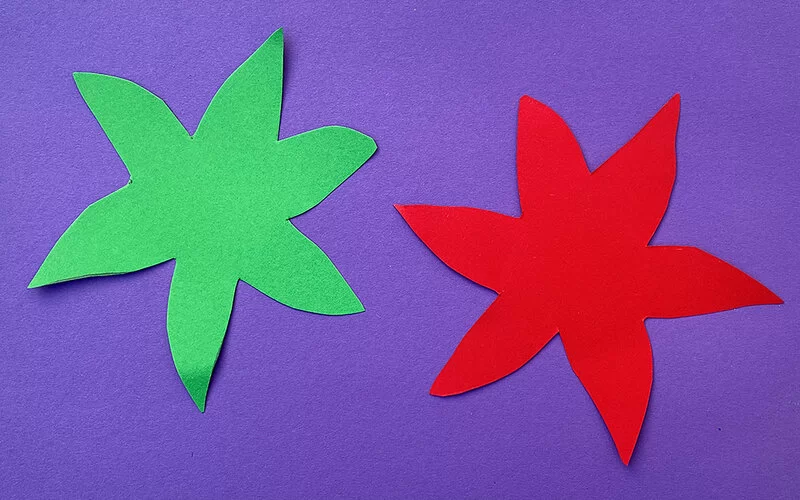 Zwei Bögen farbiges Tonpapier in Form von sechsblättrigen Seerosen, grün und rot. Der Hintergrund ist violettblau.