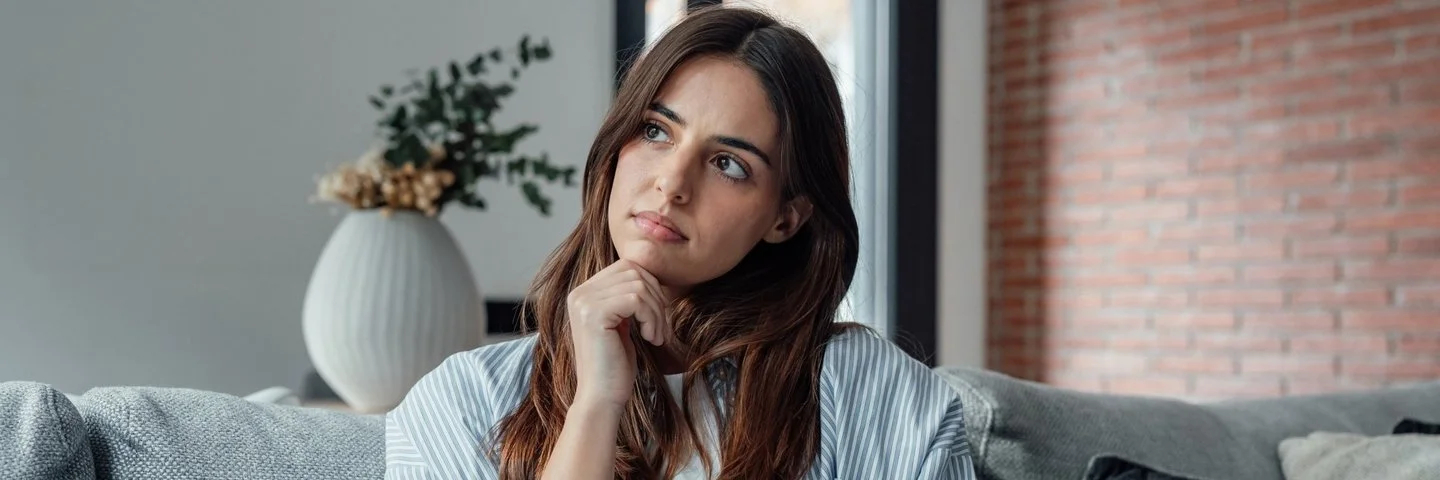 Frau sitzt nachdenklich vor ihrem Laptop auf dem Sofa