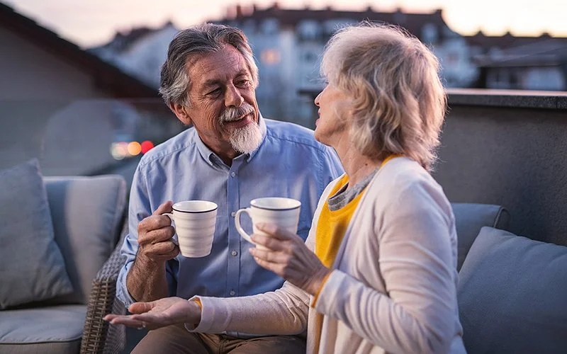 Seniorenpaar trinkt eine Tasse Tee auf ihrem Balkon in den Abendstunden.