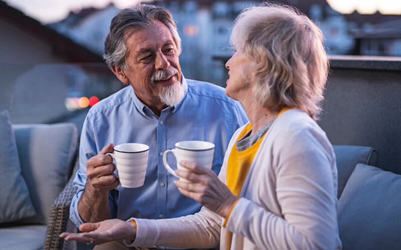 Seniorenpaar trinkt eine Tasse Tee auf ihrem Balkon in den Abendstunden.
