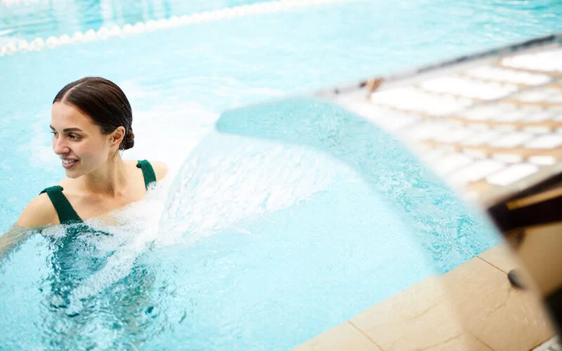 Eine Frau in einem Thermalbad steht unter einem Wasserstrahl.