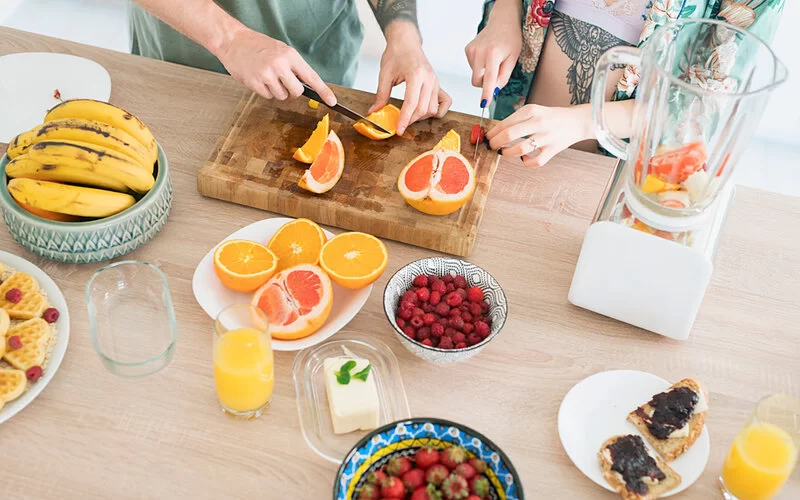 Zwei Personen schneiden Grapefruits für einen Smoothie.