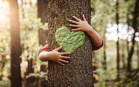Ein Kind umarmt zum Zeichen der Nachhaltigkeit einen Baum, auf den ein grünes Herz gemalt ist.