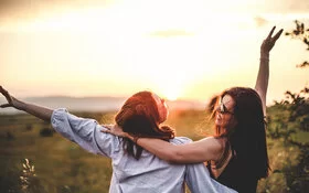 Zwei jugendliche Mädchen betrachten glücklich den Sonnenuntergang. Toxic Positivity kann auch Freundschaften belasten.