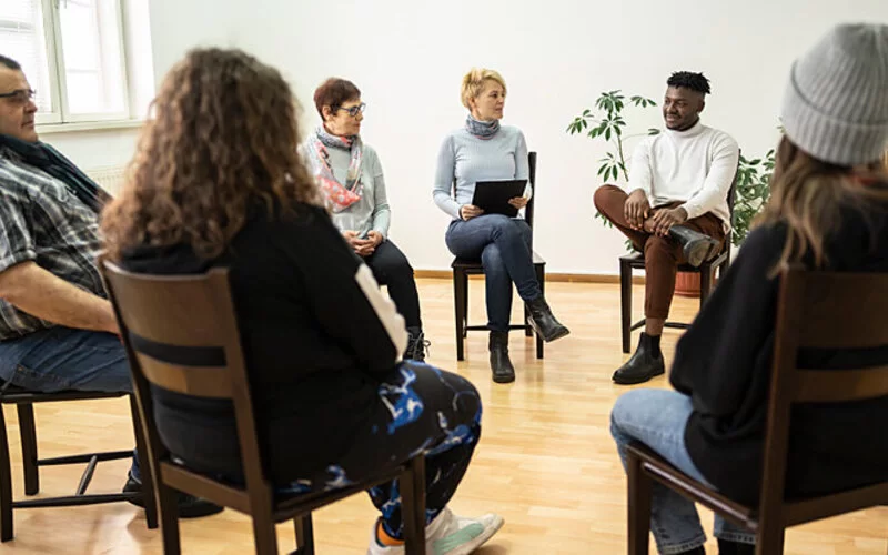 Menschen sitzen im Kreis und reden darüber, wie eine Sucht bei ihnen entstehen konnte.