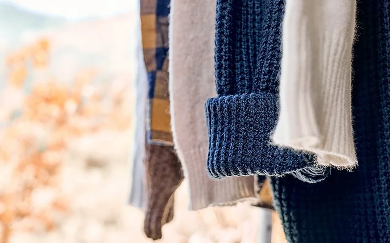 Die Ärmel verschiedener Wollpullover, die in einem herbstlichen Garten zum Lüften hängen.