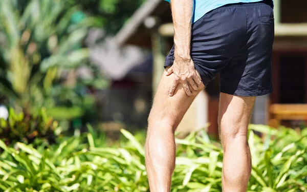 Ein Jogger greift mit der Hand an seinen schmerzenden Oberschenkel.