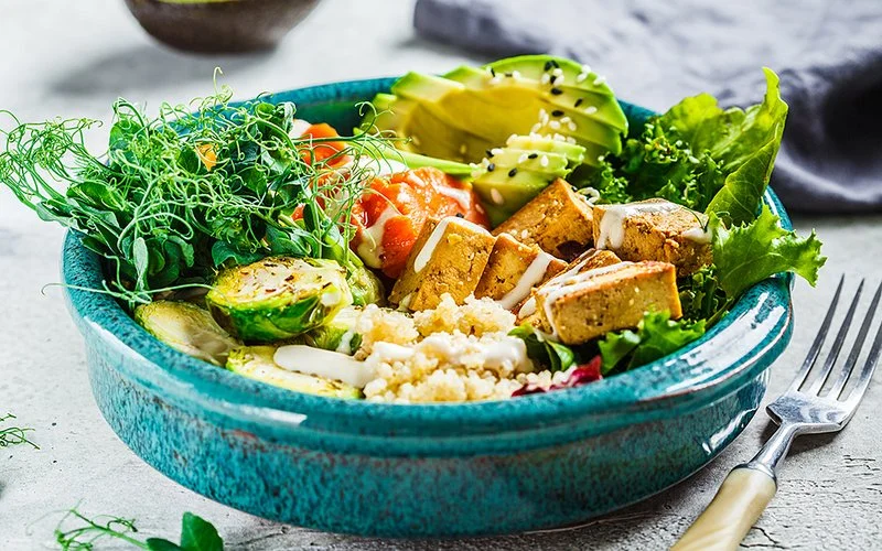 Bowl mit Tofu, Avocado, Quinoa, Süßkartoffel, Rosenkohl, Salat und Sprossen.
