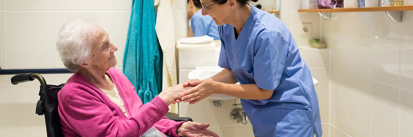 Eine Pflegekraft kümmert sich um eine Seniorin im Badezimmer.