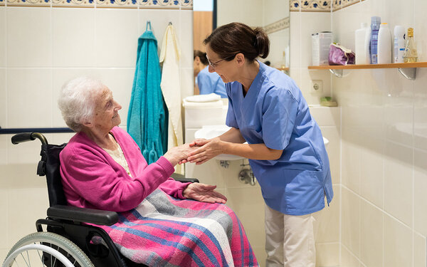 Eine Pflegekraft kümmert sich um eine Seniorin im Badezimmer.