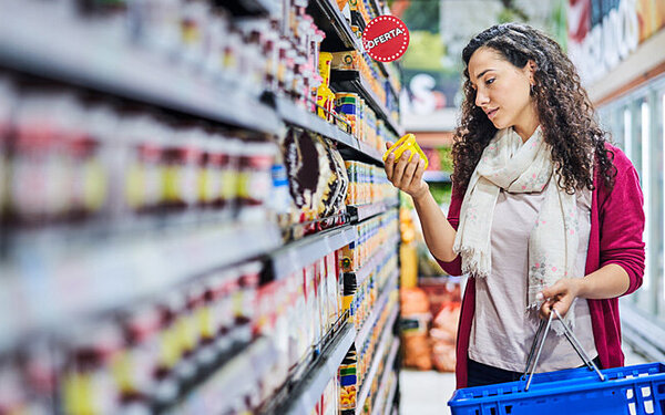 Eine junge Frau liest im Supermarkt die Zutatenliste von einem Produkt aus dem Supermarktregal.