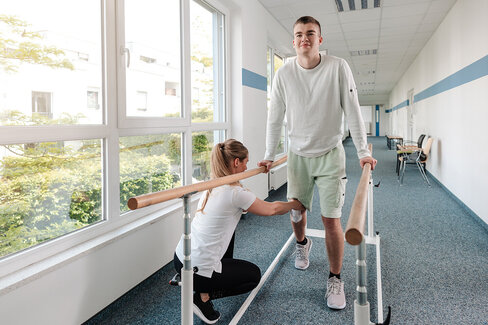 Eine Therapeutin übt mit einem jungen Mann nach einer Sportverletzung. Eine Reha kann Krankheiten lindern.