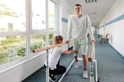 Eine Therapeutin übt mit einem jungen Mann nach einer Sportverletzung. Eine Reha kann Krankheiten lindern. 